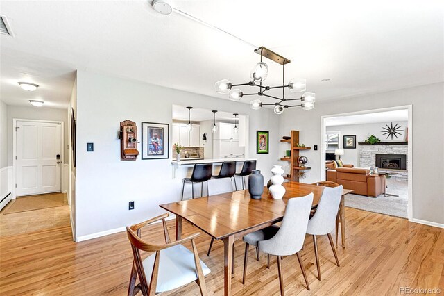 12256 W 34th Pl, Wheat Ridge, CO 80033 - dining space featuring a chandelier, light wood-style floors, baseboards, a stone fireplace, and a baseboard radiator