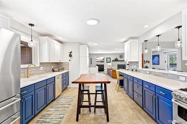 12256 W 34th Pl, Wheat Ridge, CO 80033 - kitchen with appliances with stainless steel finishes, blue cabinetry, tasteful backsplash, a sink, and a fireplace