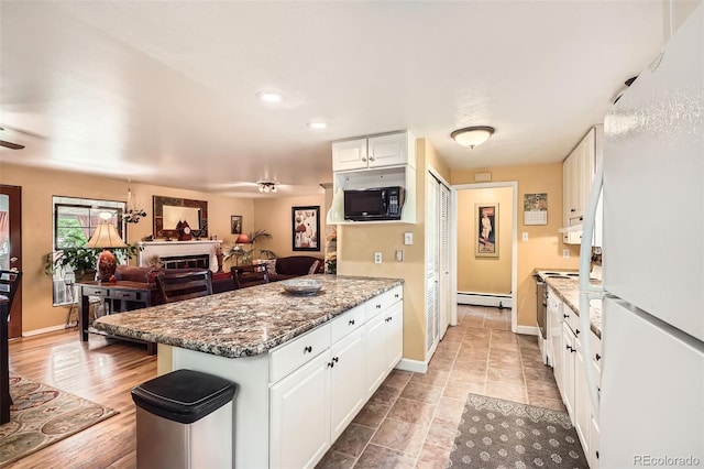 6940 W 63rd Ave, Arvada, CO 80003 - kitchen with a peninsula, a baseboard heating unit, black microwave, freestanding refrigerator, and white cabinetry