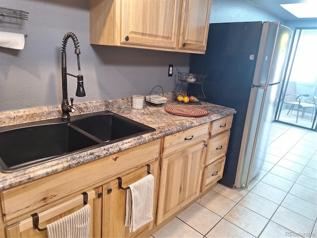 kitchen with sink, light tile patterned floors, light brown cabinetry, a skylight, and stainless steel refrigerator