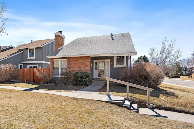 view of front of house with brick siding, a shingled roof, fence, a front lawn, and a chimney