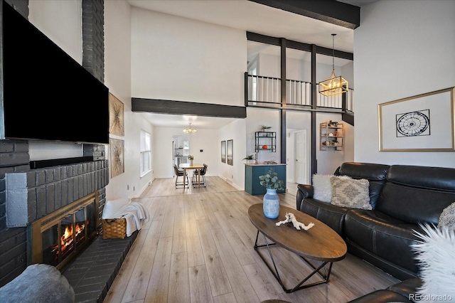 living room featuring a fireplace, high vaulted ceiling, a chandelier, beamed ceiling, and hardwood / wood-style floors