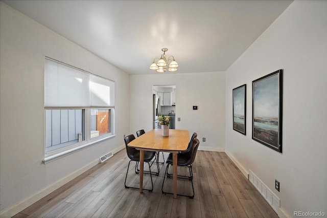 dining space featuring wood finished floors, visible vents, and an inviting chandelier