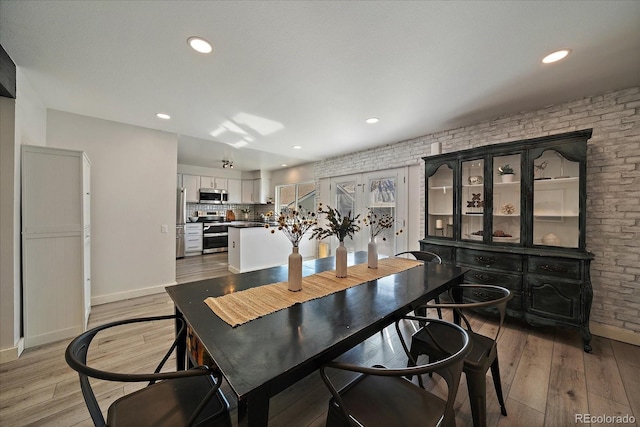 dining room with light wood finished floors, brick wall, baseboards, and recessed lighting