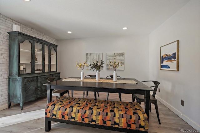 dining space featuring brick wall, recessed lighting, light wood-type flooring, and baseboards