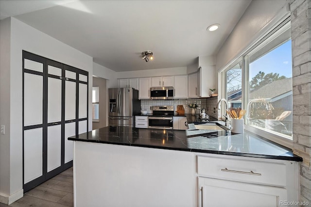 kitchen featuring tasteful backsplash, dark countertops, stainless steel appliances, white cabinetry, and a sink