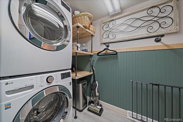 washroom with stacked washer / drying machine, laundry area, a wainscoted wall, and wood finished floors