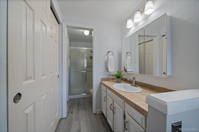 bathroom featuring toilet, a shower stall, wood finished floors, and vanity