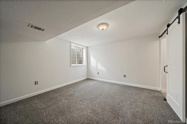 interior space with a barn door, visible vents, baseboards, carpet, and a textured ceiling