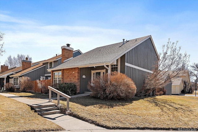 mid-century modern home with a shingled roof, brick siding, a chimney, and a front lawn