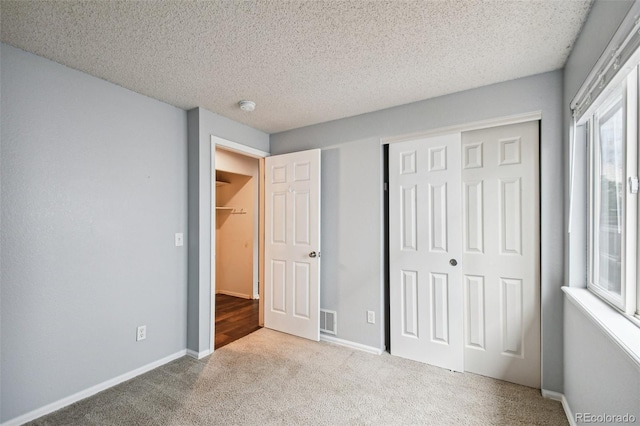 unfurnished bedroom with multiple windows, light colored carpet, a closet, and a textured ceiling