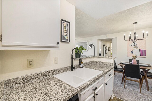 kitchen with light stone countertops, a textured ceiling, sink, an inviting chandelier, and white cabinetry