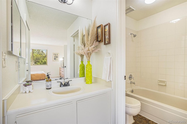 full bathroom featuring a textured ceiling, vanity, toilet, and tiled shower / bath