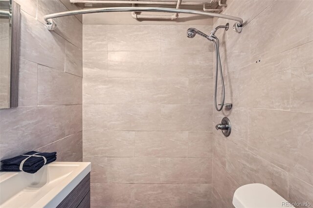 bathroom with a tile shower, toilet, and vanity