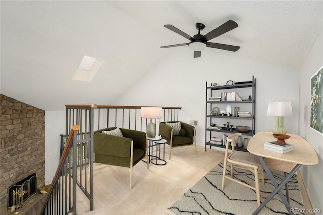 sitting room featuring vaulted ceiling with skylight, a fireplace, light colored carpet, and ceiling fan