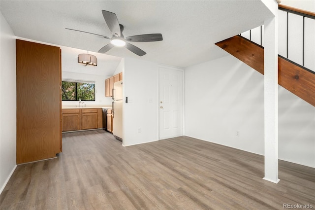 unfurnished living room with sink, vaulted ceiling, a textured ceiling, light hardwood / wood-style floors, and ceiling fan