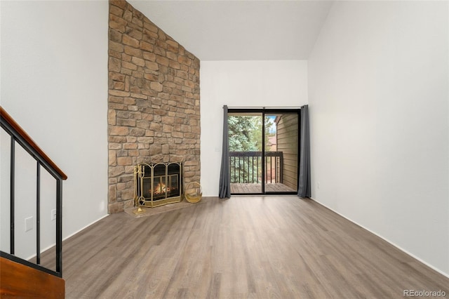 unfurnished living room featuring hardwood / wood-style flooring, vaulted ceiling, and a stone fireplace