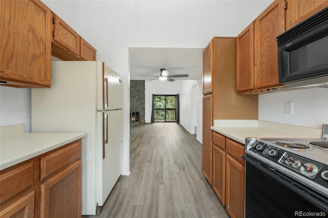 kitchen with light hardwood / wood-style floors, a stone fireplace, black appliances, and ceiling fan