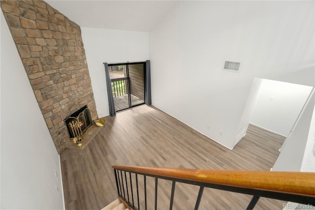 unfurnished living room featuring a stone fireplace, lofted ceiling, hardwood / wood-style flooring, and heating unit