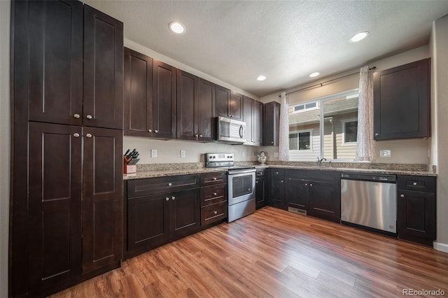 kitchen featuring a sink, appliances with stainless steel finishes, light wood-style flooring, and dark brown cabinetry