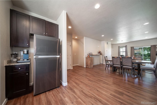 kitchen with light stone countertops, light wood-style flooring, dark brown cabinets, and freestanding refrigerator