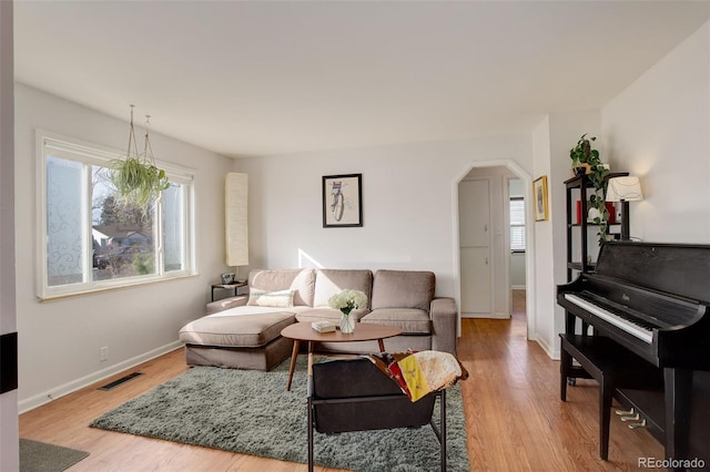 living area with visible vents, arched walkways, light wood-style floors, and baseboards