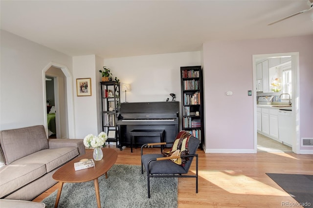 living area with arched walkways, baseboards, and light wood-style floors