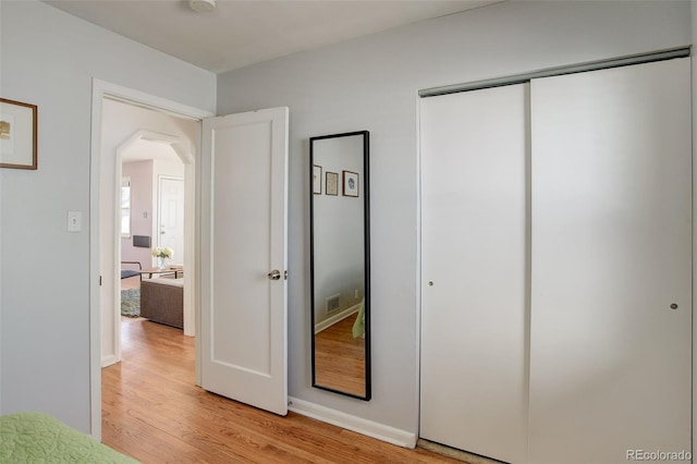 unfurnished bedroom featuring a closet, arched walkways, and light wood finished floors