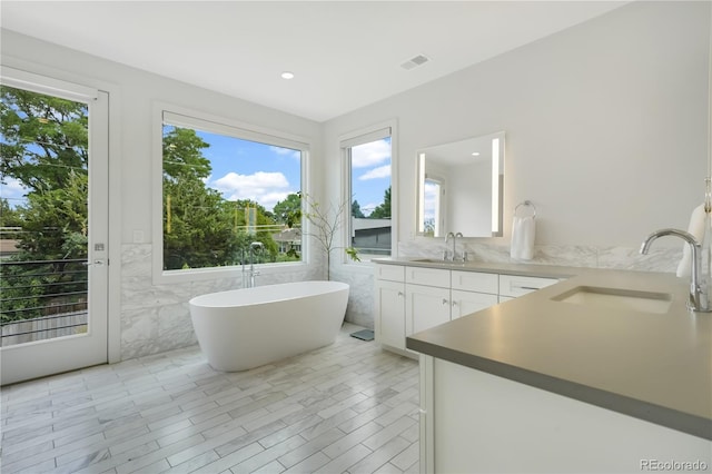 3450 S Cherry St, Denver, CO 80222 - full bathroom featuring tile walls, double vanity, plenty of natural light, a freestanding bath, and recessed lighting