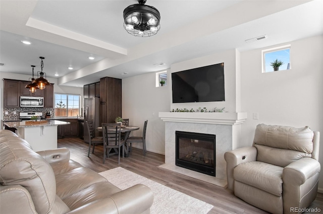 living area with a fireplace, light wood finished floors, recessed lighting, visible vents, and baseboards