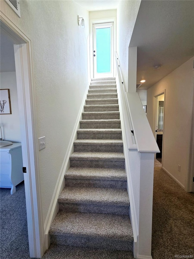 staircase with a textured wall, carpet flooring, visible vents, and baseboards