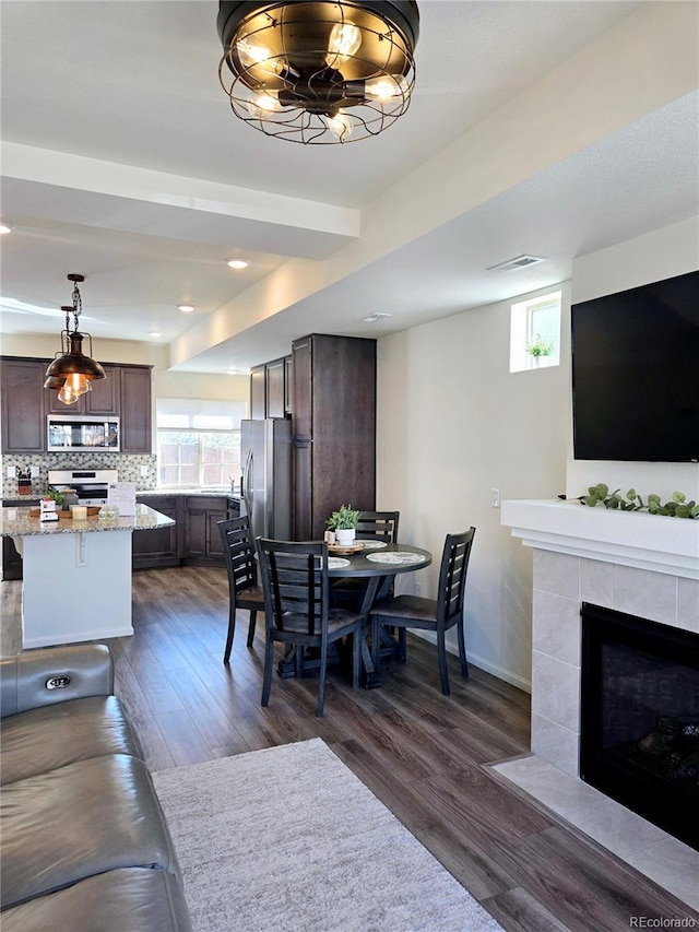 dining space featuring dark wood-type flooring, baseboards, and a tiled fireplace