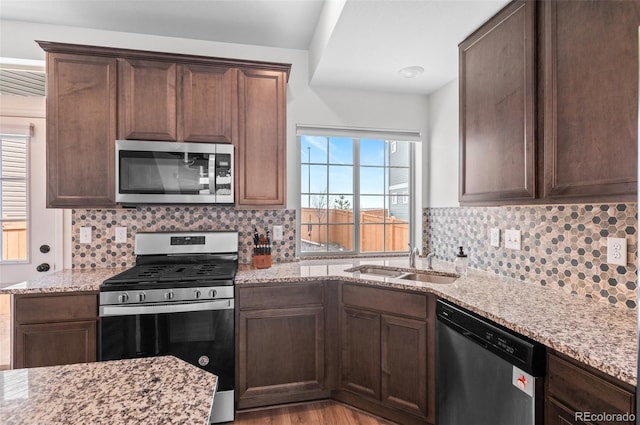 kitchen with appliances with stainless steel finishes, a sink, decorative backsplash, and light stone counters