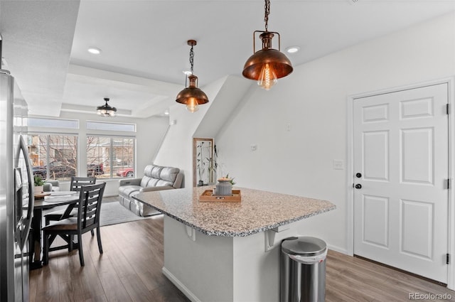 kitchen with light stone counters, dark wood-style flooring, hanging light fixtures, stainless steel refrigerator with ice dispenser, and a center island