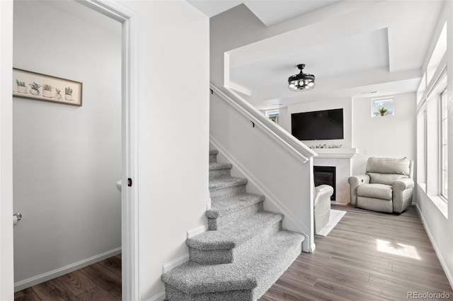 staircase featuring a fireplace, baseboards, and wood finished floors