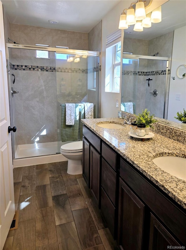 full bathroom featuring double vanity, toilet, wood tiled floor, a sink, and a shower stall