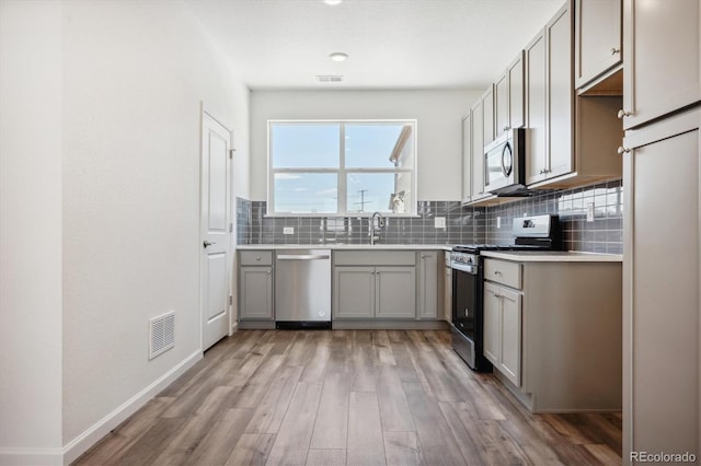 kitchen with gray cabinets, appliances with stainless steel finishes, sink, decorative backsplash, and light hardwood / wood-style flooring