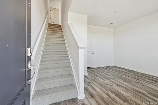 stairway featuring wood finished floors, visible vents, and baseboards