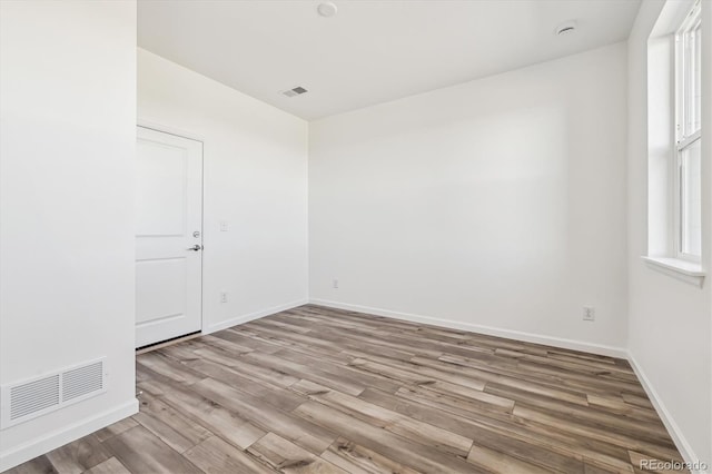 empty room with wood finished floors, visible vents, and baseboards