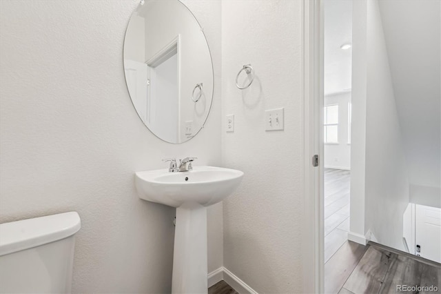 half bath with toilet, baseboards, wood finished floors, and a textured wall