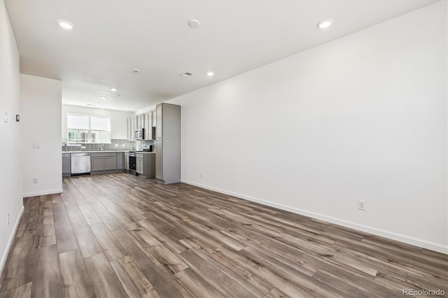 unfurnished living room featuring dark wood-style flooring, recessed lighting, a sink, and baseboards