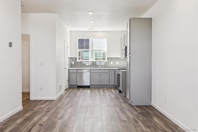 kitchen featuring tasteful backsplash, baseboards, appliances with stainless steel finishes, wood finished floors, and gray cabinets