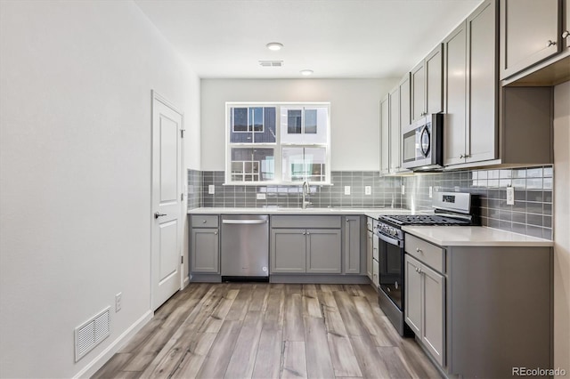 kitchen with visible vents, appliances with stainless steel finishes, a sink, gray cabinetry, and backsplash