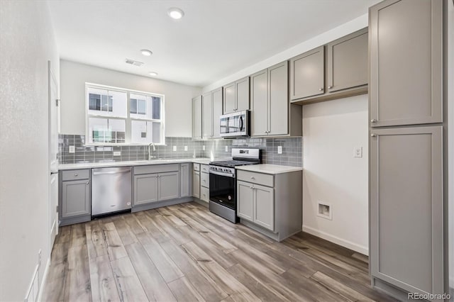 kitchen featuring stainless steel appliances, backsplash, gray cabinets, and visible vents