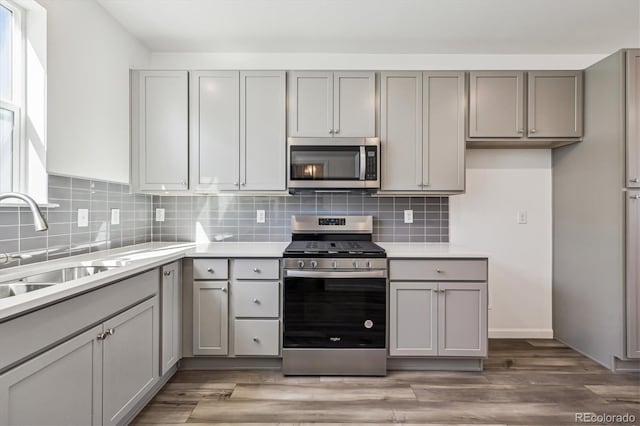 kitchen featuring tasteful backsplash, gray cabinetry, appliances with stainless steel finishes, light wood-style floors, and a sink