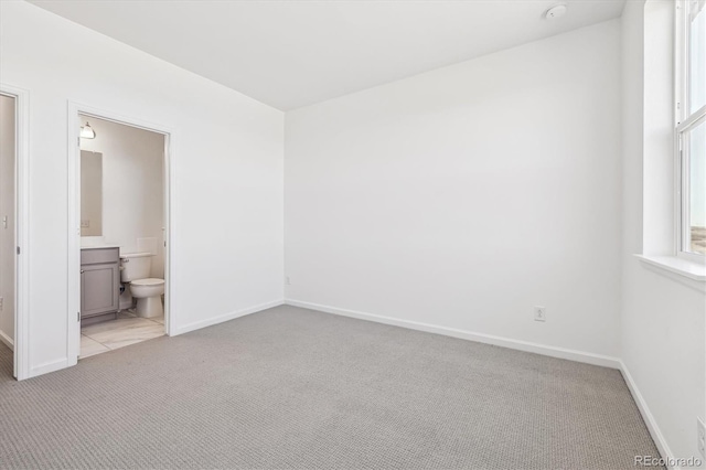 unfurnished bedroom with baseboards, connected bathroom, and light colored carpet