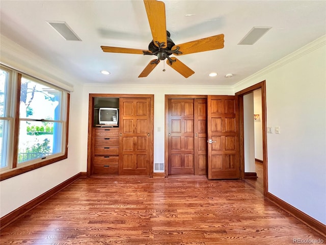 unfurnished bedroom featuring crown molding, baseboards, wood finished floors, and visible vents