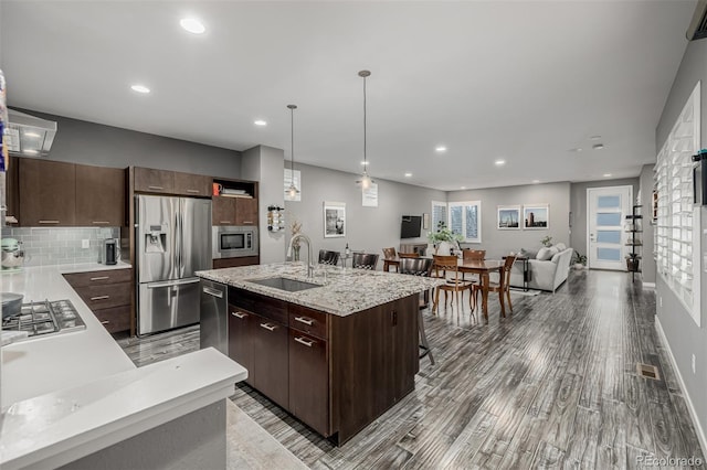 kitchen featuring a breakfast bar, an island with sink, a sink, tasteful backsplash, and appliances with stainless steel finishes