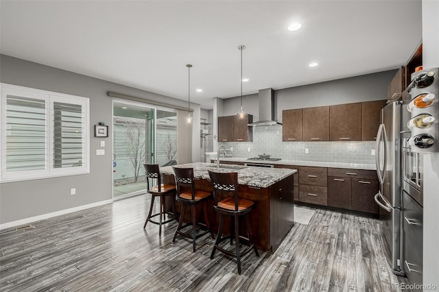 kitchen with tasteful backsplash, a breakfast bar area, appliances with stainless steel finishes, wall chimney exhaust hood, and a sink