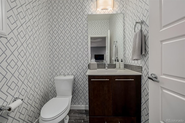 bathroom featuring toilet, vanity, and wallpapered walls